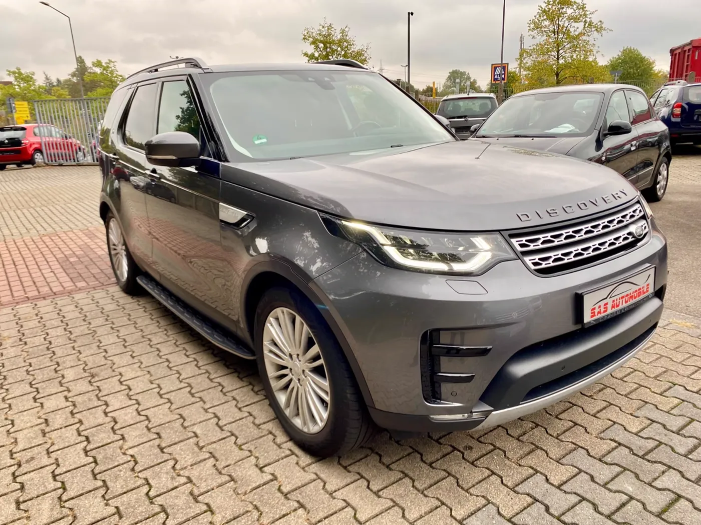 Grauer Land Rover Discovery 5 HSE, schräg von vorn, auf dem Hof von S.A.S Automobile